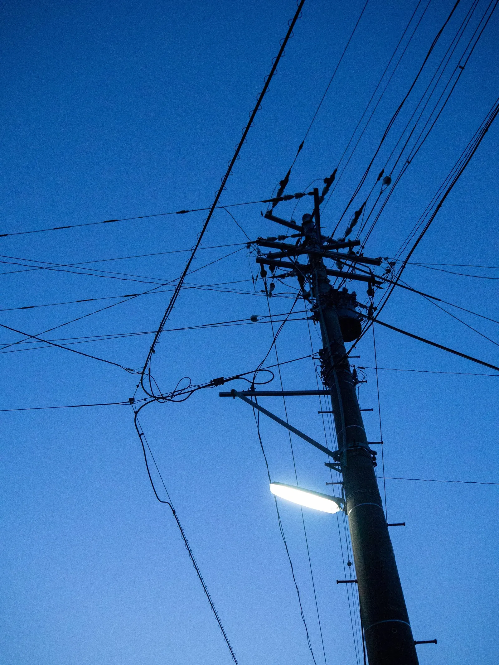 A utility pole and tangled wires against a deep blue evening sky