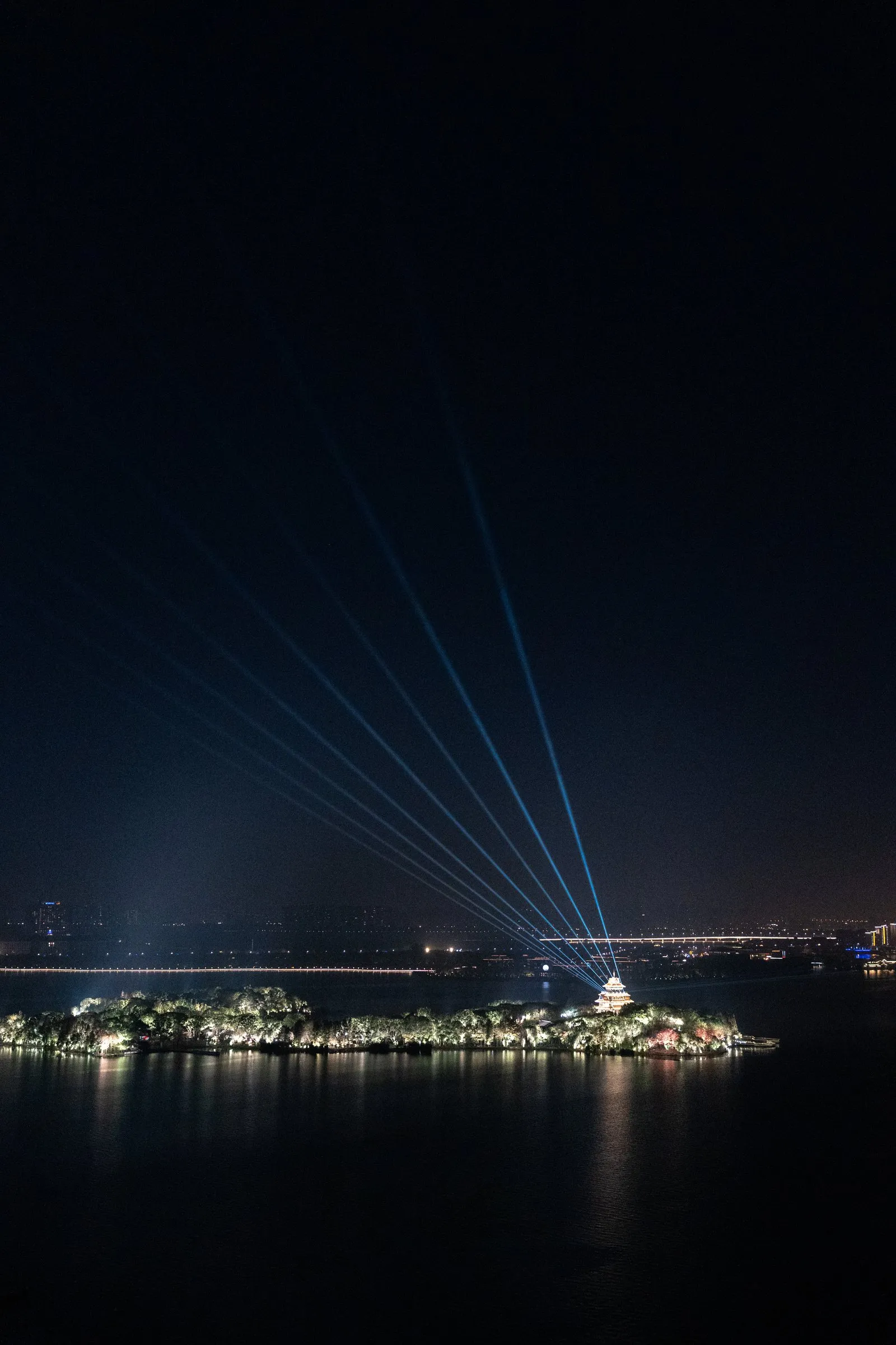 Light beams fanning over a lake island pagoda at night